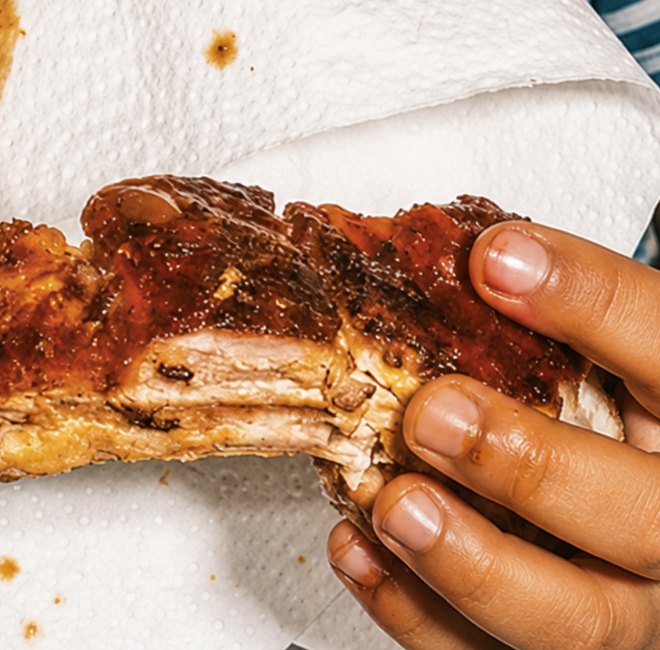 A child's hands gripping a piece of glazed roasted meat, fingers deep in the sticky sauce