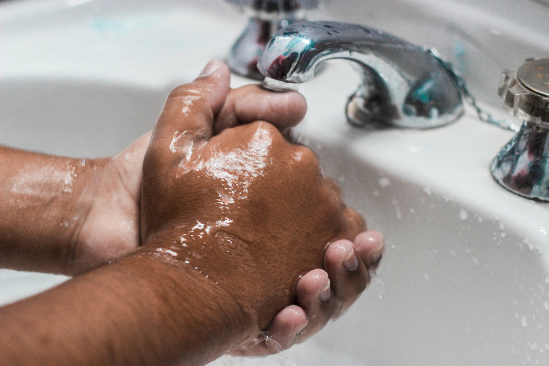 Two hands being scrubbed together under a running tap at a white sink